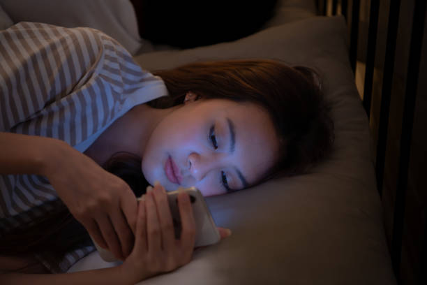 portrait d’une belle femme asiatique utilisant un téléphone portable sur le lit la nuit - sleeping lying on back couple bed photos et images de collection