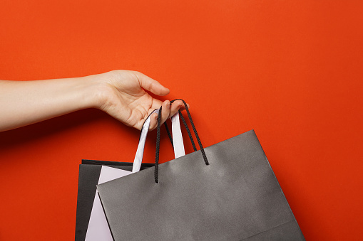 Big sale, low prices. Female hand holds black paper shopping bags on a red background, copy space. Black Friday concept
