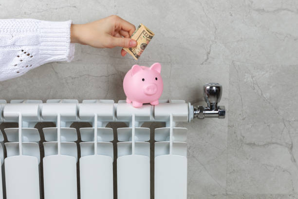Savings concept.Money in piggy bank on radiator on a gray wall background. Concept of heating season. Concept of expensive heating costs and rising energy bill prices for winter cold season. concepto de ahorro. dinero en alcancía en radiador sobre fondo de pared gris. concepto de temporada de calefacción. concepto de costos de calefacción caros y aumento de los precios de las facturas de energía para la temporada de frío de invierno.