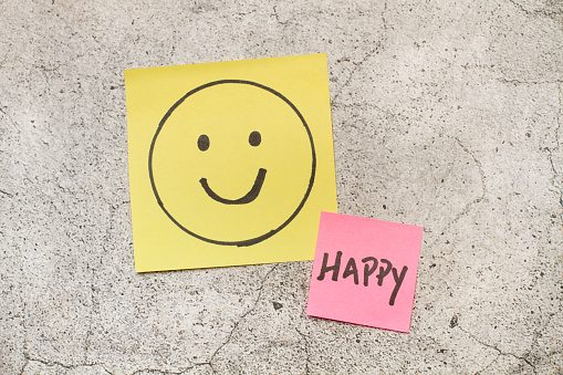 Colored paper notes with happy drawing face and single word on a gray marble background