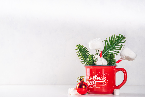 Santa`s stuck in the chimney hot chocolate, Funny Christmas cocoa mug with marshmallow and straw made like Santa`s legs, with Christmas tree, bauble and decor, on white bokeh background copy space