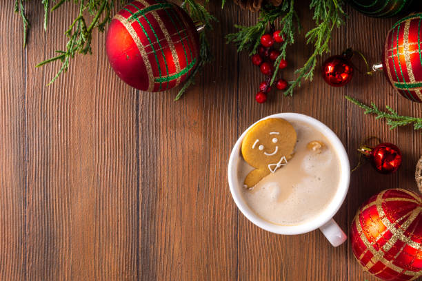 Funny cute gingerbread man in a hot chocolate, cappuccino or latte. Festive Christmas cocoa mug with marshmallow and cookie, with Christmas tree, decor, on white bokeh background copy space