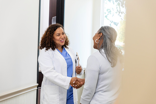 The senior adult woman stops to shake the mid adult doctor's hand and thank her for her excellent care.