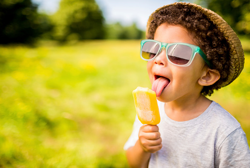 Niño en gafas de sol y sombrero comer popsicle al aire libre photo