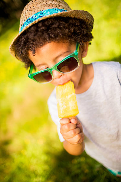 niño con gafas de sol y sombrero comer popsicle - ice cream licking little boys ice cream cone fotografías e imágenes de stock