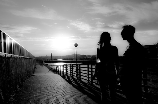 Gardony, Hungary - June 20, 2014: Sihlouette about a couple standing on a bridge and talking to each other. Black and white photo in a sunny summer day, with clouds in the sky