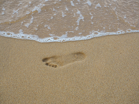 A footprint on the sand near the sea foam at the beach.