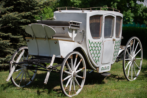 An antique white carriage from the nineteenth century on a green lawn. The prototype of a modern car.
