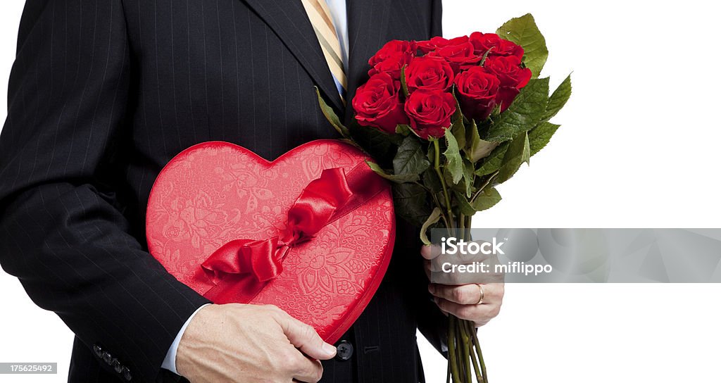 Man holding roses and red heart with chocolates on white A man in a suit holding red roses and a red heart with chocolates on a white background with copy space Blossom Stock Photo