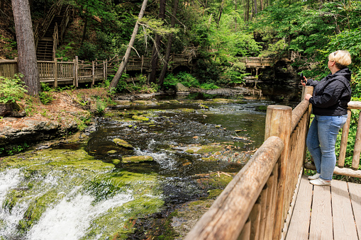Tourist woman captures Bushkill Falls cascade on camera from wooden trail at Bushkill Falls, Pocono Mountains in Pennsylvania
