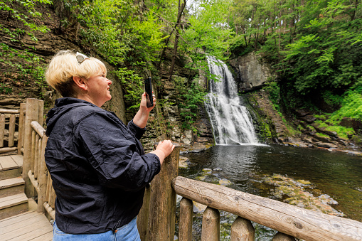 Waterfall landmark in Poconos Mountains, PA. Mature blonde woman – tourist taking photos during hiking in Bushkill Falls in Pennsylvania