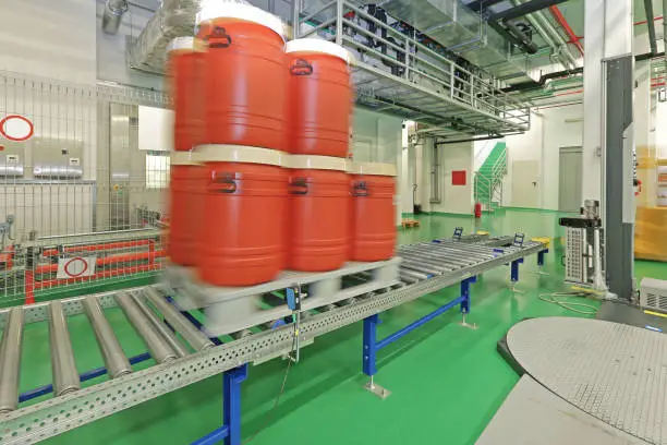 Plastic Barrels Moving at Automated Storage Gravity Conveyor in Chemical Warehouse