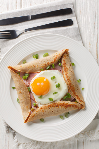 Buckwheat galettes with egg, ham, and cheese make an incredibly satisfying brunch with their savory and nutty flavor closeup on the plate on the table. Vertical top view from above