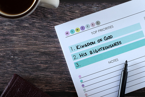 Christian top priorities list, seek first kingdom of God and His righteousness, handwritten text in notebook with cup of coffee and holy bible book on wood