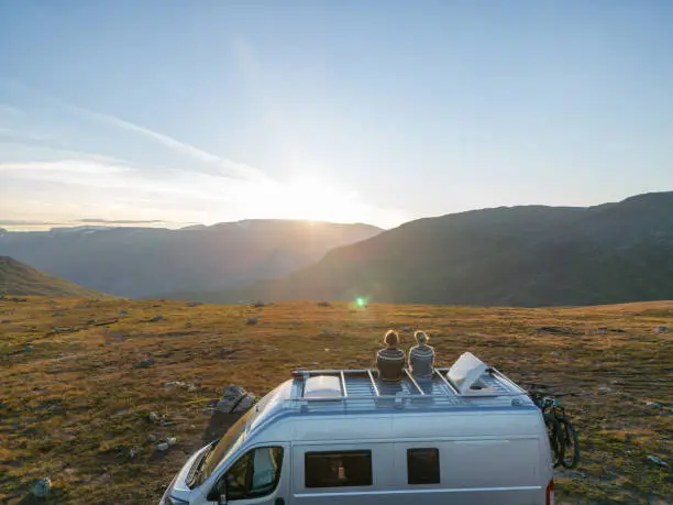 Photo of Drone shot Road trip concept- Couple on the roof of a motorhome watching sunset, autumn