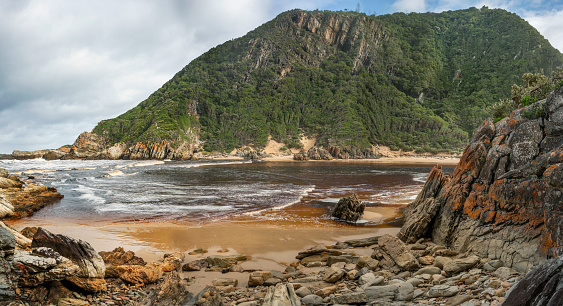 Scenic view of a small beach with calm water looking out at mountains on a rugged coastline by the ocean