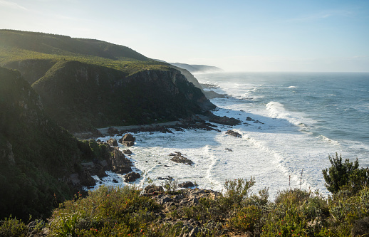 Scenic view from a mountain of a rocky coastline by the ocean with ocean waves on sunny day