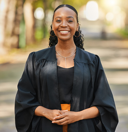 Portrait of a happy African American young woman in graduation gown holding a diploma and enjoying after graduating