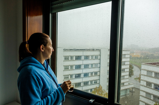 woman looking out the window with a coffee in her hand in rainy weather