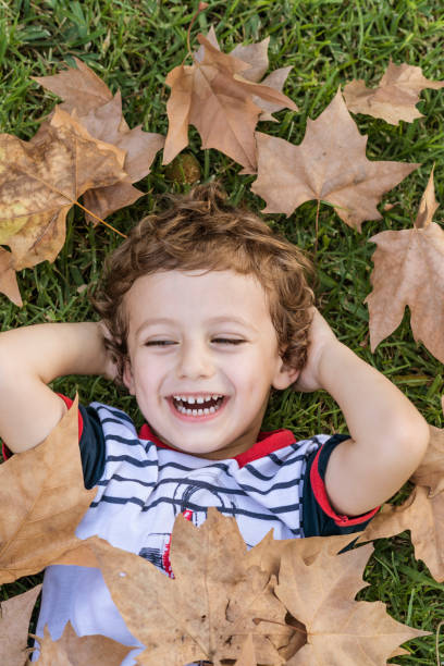 istock Child lying on the grass surrounded by fallen autumn leaves. 1756330878
