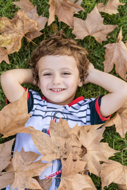 istock Child lying on the grass surrounded by fallen autumn leaves. 1756330886
