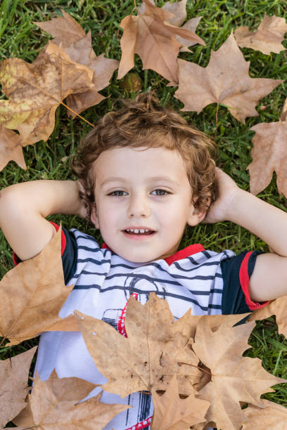 istock Child lying on the grass surrounded by fallen autumn leaves. 1756330887