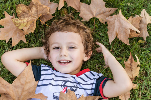 istock Child lying on the grass surrounded by fallen autumn leaves. 1756330889