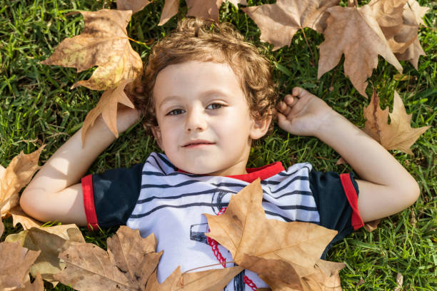 istock Child lying on the grass surrounded by fallen autumn leaves. 1756330903