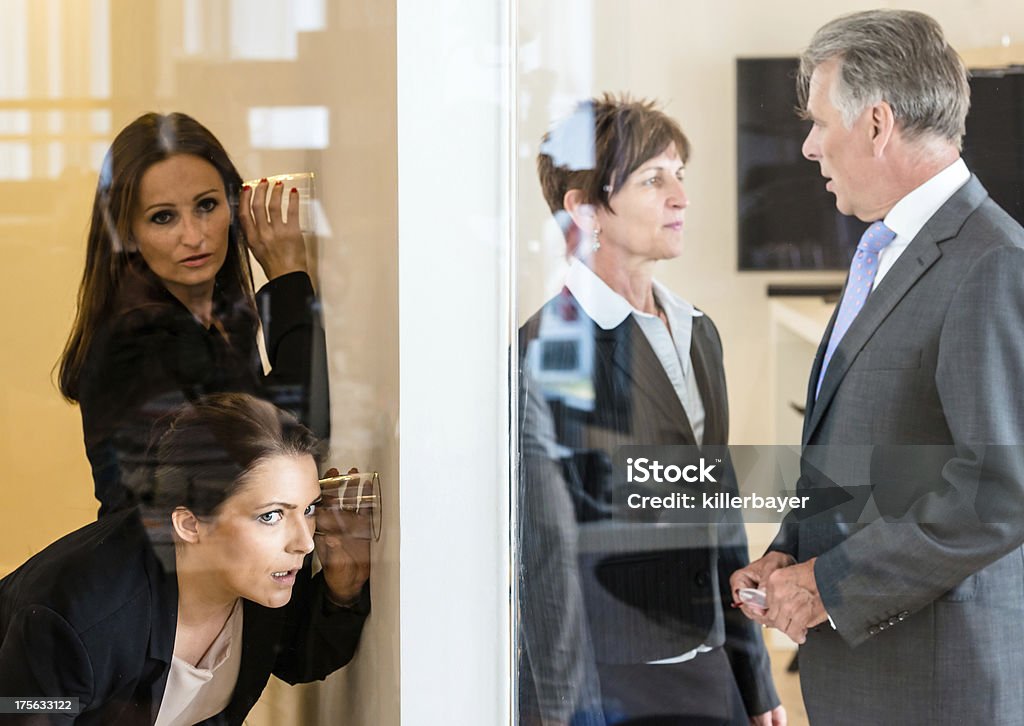 eavesdropping in the office Two colleagues listening with a glass to the wall of the next office room where a man and a woman discuss their matters. Concept for eavesdropping, secrecy or curiosity Adult Stock Photo