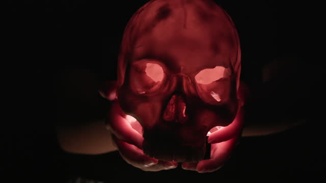 Close-up young girl hand holds glowing light of Skull in the dark on Halloween night, Halloween party concept.