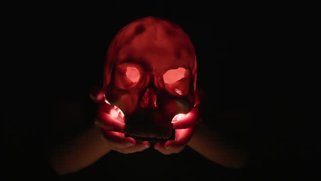 Close-up young girl hand holds glowing light of Skull in the dark on Halloween night, Halloween party concept.