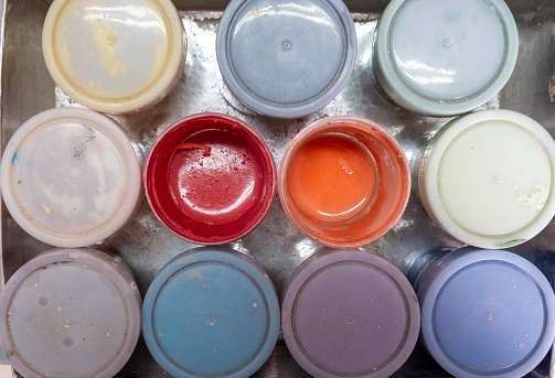 Top view of ceramic glazes in a box. The lids are closed except for the red and orange ones.