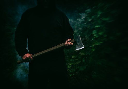 A man with an ax in his hands close-up against the background of smoke at night in the forest.