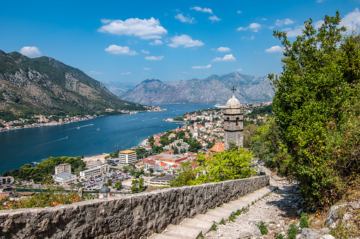Travel image of Kotor bay and city with staircase, historic walls and church. Mountains in the background. Popular cruise destination in Europe. Unesco World Heritage site.