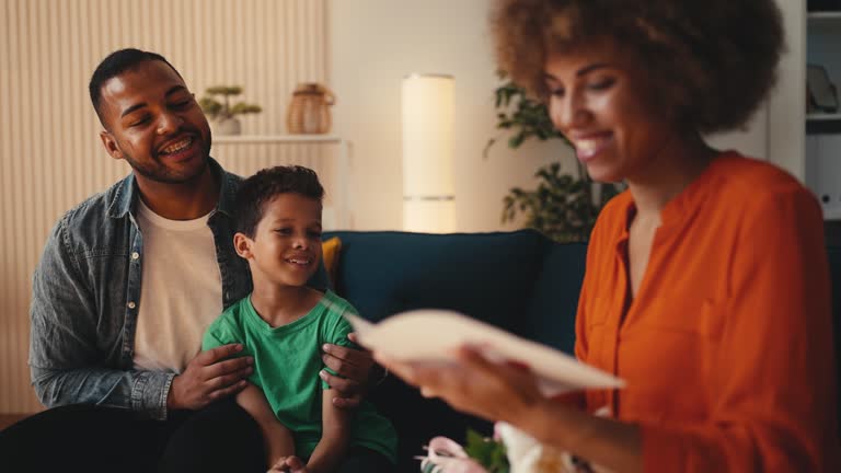 Boy and father greeting mom on Mother's day with a card, flowers and a gift