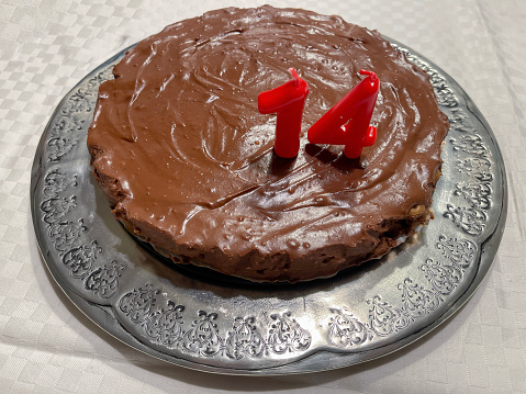 a simple and delicious cookie and chocolate cake on a silver platter on a white tablecloth, with a fourteenth birthday candle, horizontal