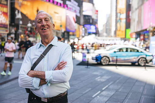 A white senior man posing looking at camera outdoors in New York City streets.
