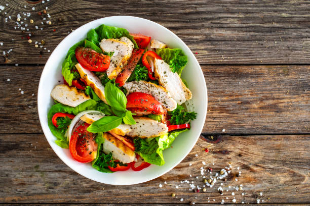 Caesar style salad  - fresh vegetables with grilled sliced chicken breast on wooden table