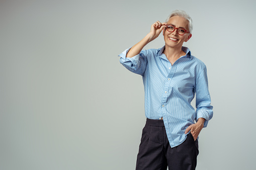 Portrait of smiling senior woman wearing red stylish eyeglasses looking at camera on the grey background. Successful business concept