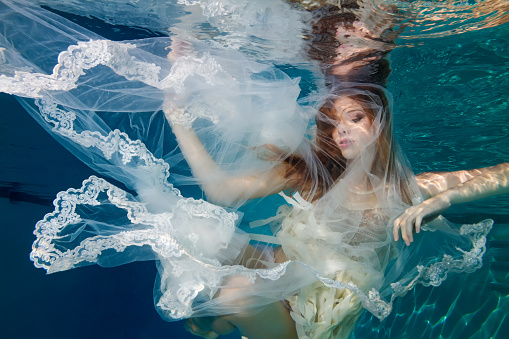 A woman is caught in a net underwater, the net is a wedding veil which could symbolize being stuck in an unhappy marriage. She appears content to be in her position.