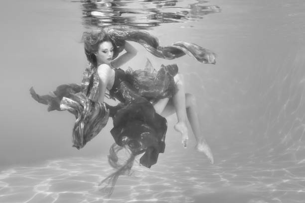 A woman appears to be floating underwater with a reflection above, the ethereal dress weightless around her.