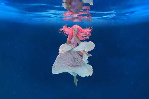 A woman with pink hair appears to be an underwater fairy