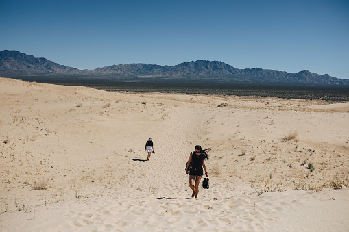 Women enjoying the vast wilderness of the Mojave desert, walking barefoot  through the hot sand, carrying a camera, experiencing the amazing nature of the American West.