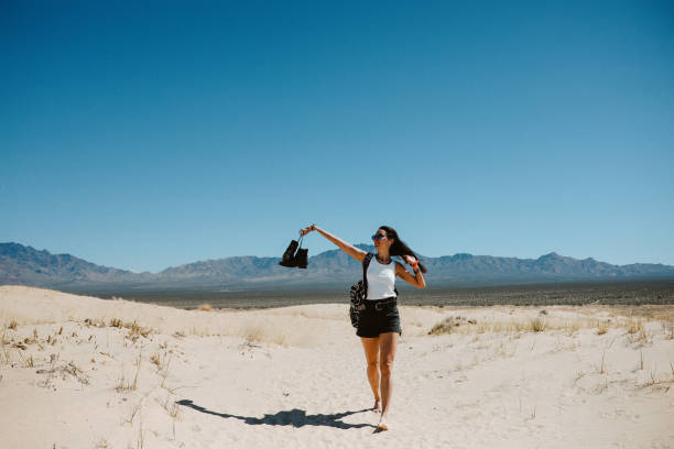 Woman enjoying the vast wilderness of the Mojave desert, walking barefoot  through the hot sand, carrying a camera, experiencing the amazing nature of the American West.