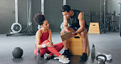 Personal trainer, woman and man with schedule for exercise, chart plan or check fitness progress in gym. Sports instructor, coach and checklist of people training for body health, workout or wellness