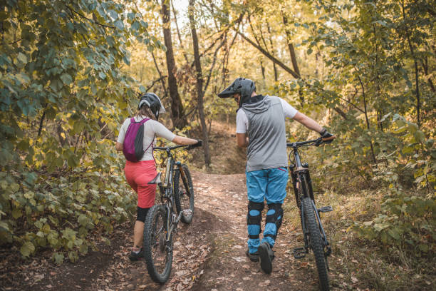 istock Back view of two friends with helmets pushing bicycles and walking through the forest until they reach a point from which they will go downhill 1756528428