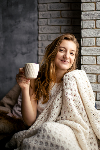 A cheerful young lady holds a coffee cup, her smile mirroring the warmth of her drink. This picture embodies the comfort of morning rituals and the joy of caffeine
