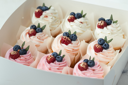 Set of cupcakes with pink and white whipped cream tops decorated with blueberries and raspberries covered with gold in a white gift box. Tasty Valentine's Day present.