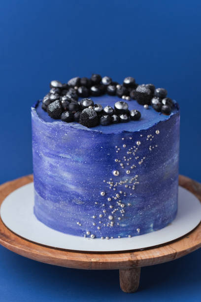 Birthday cake with blue cream cheese frosting decorated with blueberries covered with silver kandurin. Cosmic cake or space themed cake on blue background.