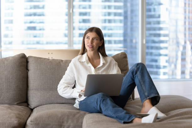 istock Woman put laptop on laps, pondering ideas seated on couch 1756587910